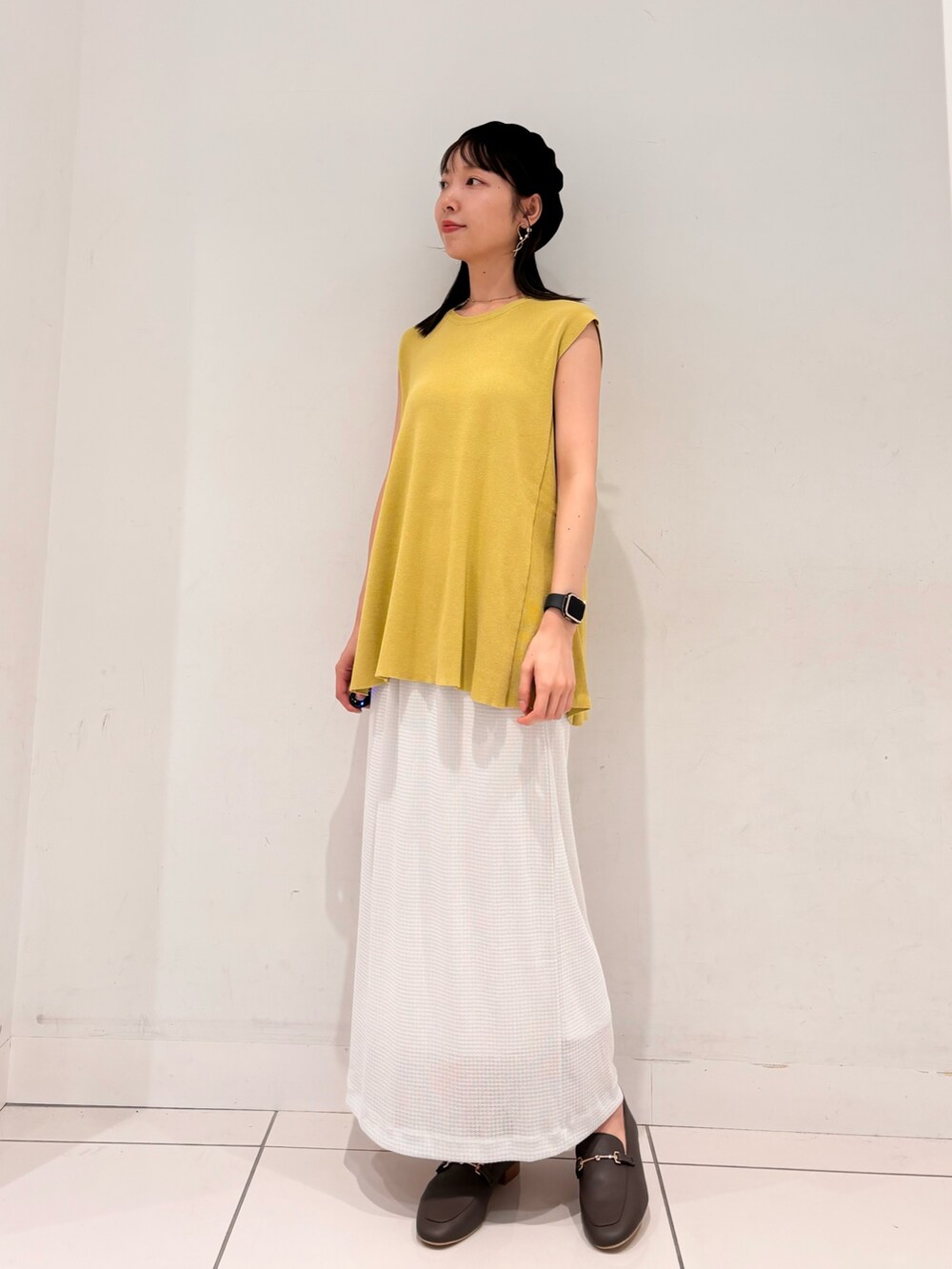 イエロー系のニット/セーター、ブラウン系のハンドバッグ、ホワイト系のスカートを着用したレディースの夏コーディネートの4枚目の写真