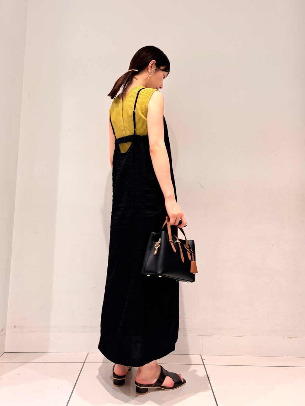 イエロー系のニット/セーター、ブラック系のワンピース、ブラック系のハンドバッグを着用したレディースの夏コーディネートの2枚目の写真
