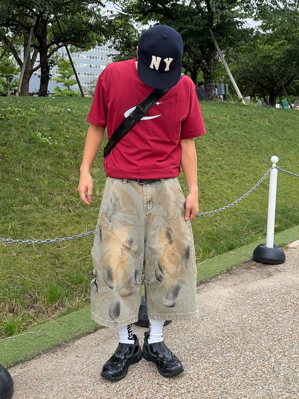 レッド系のTシャツ/カットソー、ブルー系のデニムパンツ、ブラック系のスニーカーを着用したメンズの夏コーディネートの2枚目の写真