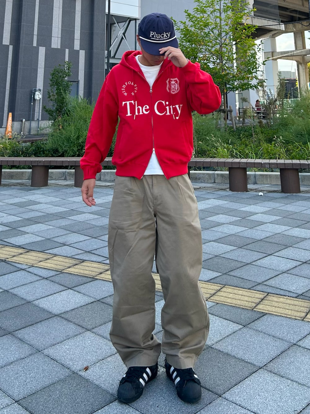 レッド系のパーカー、ベージュ系のデニムパンツ、ブラック系のスニーカーを着用したメンズの秋コーディネートの2枚目の写真