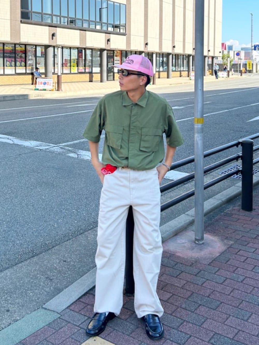 グリーン系のトップス、ベージュ系のデニムパンツ、ピンク系のキャップを着用したメンズの秋コーディネートの2枚目の写真