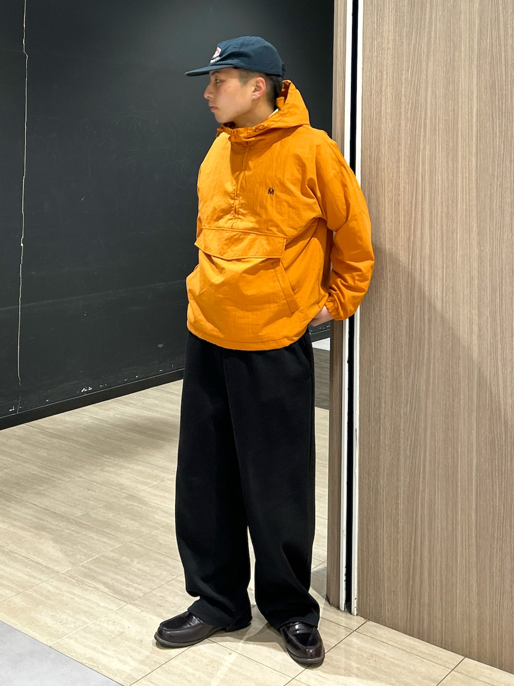 オレンジ系のマウンテンパーカー、ブラック系のスウェットパンツ、ブラウン系のローファーを着用したメンズの春コーディネートの2枚目の写真