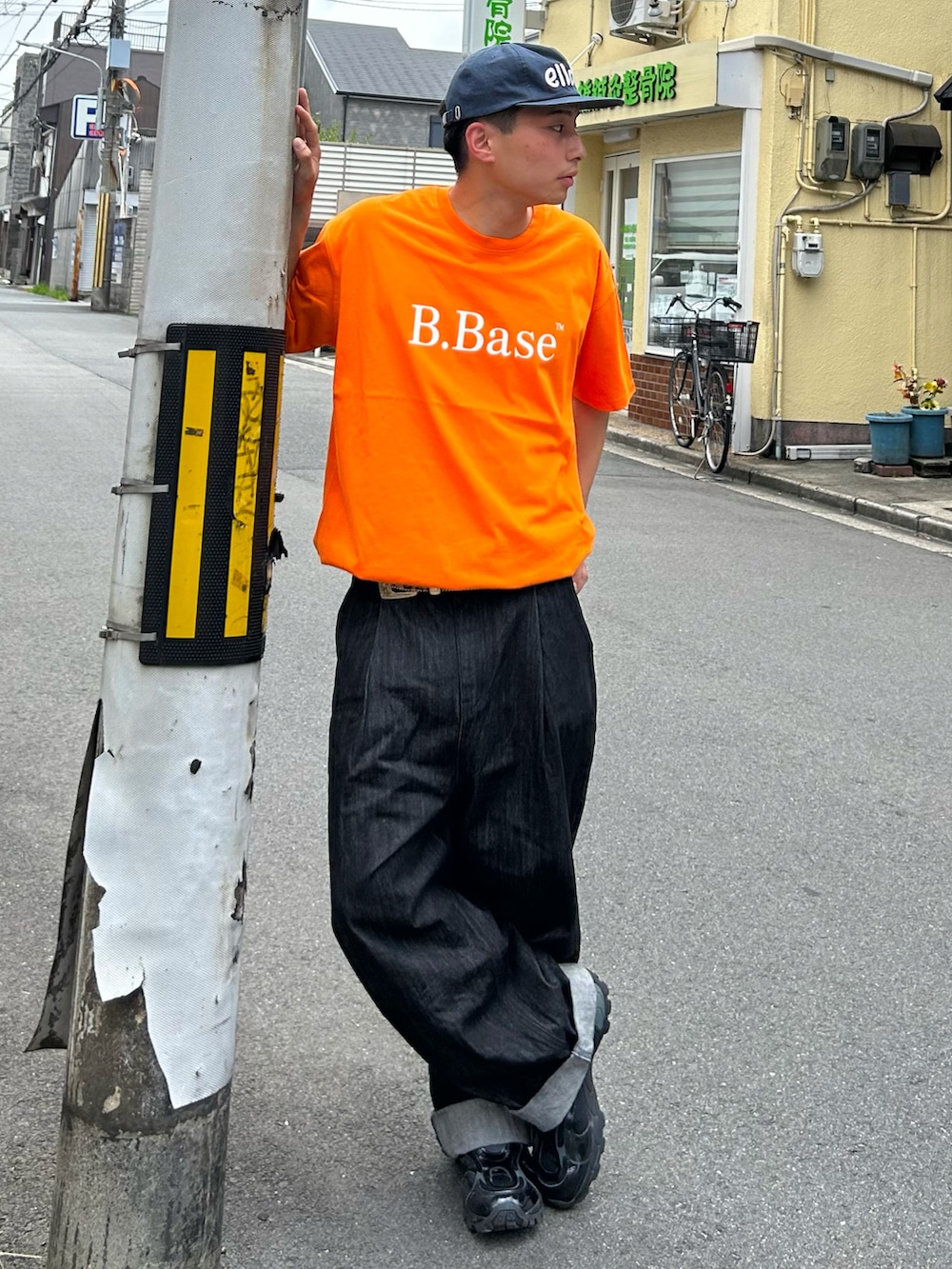 オレンジ系のTシャツ/カットソー、ブラック系のデニムパンツ、ブラック系のスニーカーを着用したメンズの夏コーディネートの2枚目の写真