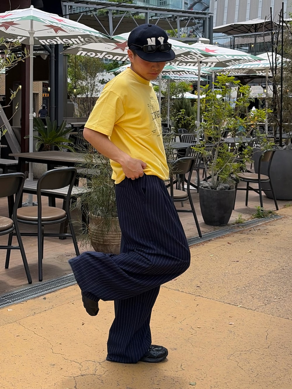 イエロー系のTシャツ/カットソー、ブルー系のスラックス、ブラック系のスニーカーを着用したメンズの夏コーディネートの2枚目の写真