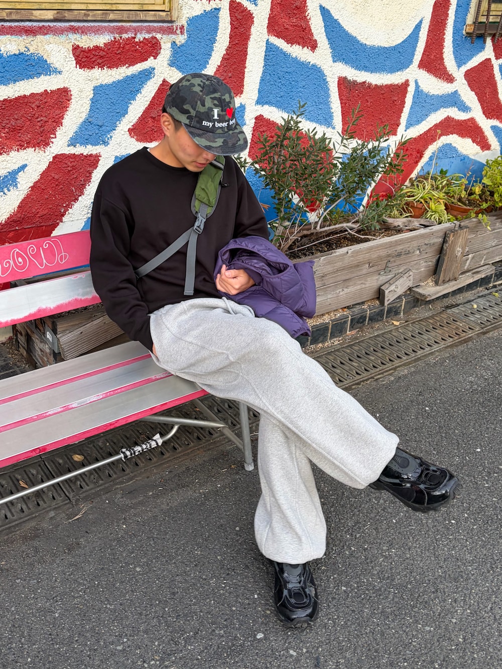 ブラック系のスウェット、パープル系のダウンベスト、グレー系のスウェットパンツを着用したメンズの冬コーディネートの3枚目の写真