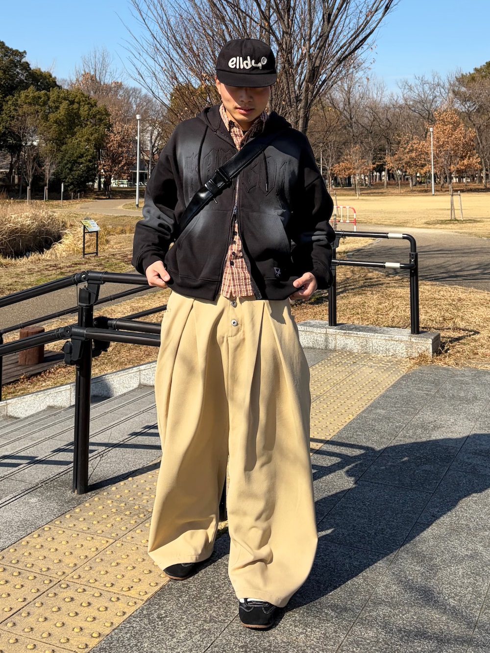 ブラック系のパーカー、ベージュ系のスラックス、ブラック系のスニーカーを着用したメンズの冬コーディネートの2枚目の写真