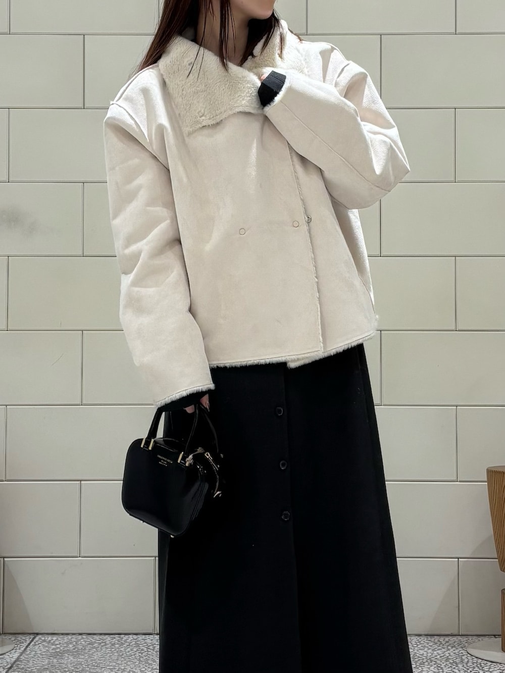 グレー系のワンピース、ホワイト系のブルゾン、ブラック系のショルダーバッグを着用したレディースの冬コーディネートの3枚目の写真