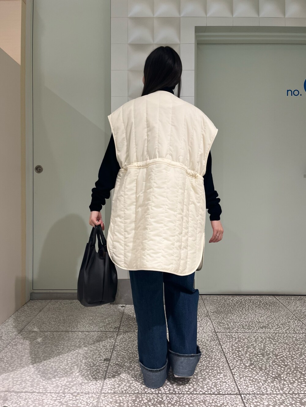 ホワイト系のダウンベスト、ブラック系のニット/セーター、ブルー系のデニムパンツを着用したレディースの秋コーディネートの4枚目の写真