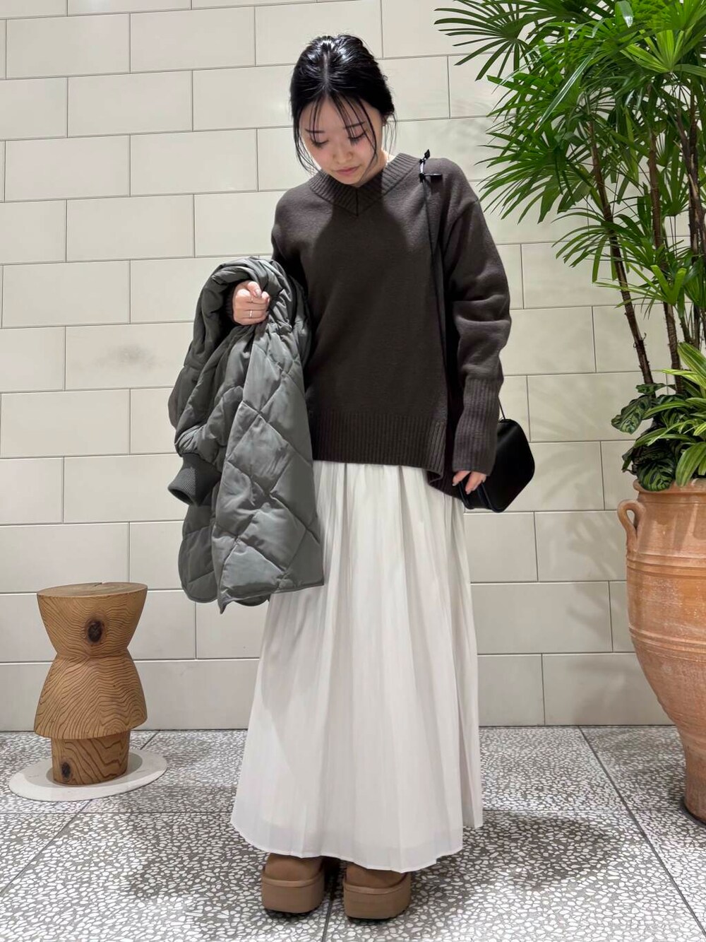 ブラウン系のニット/セーター、ホワイト系のスカート、グレー系のダウンジャケット/コートを着用したレディースの冬コーディネートの2枚目の写真