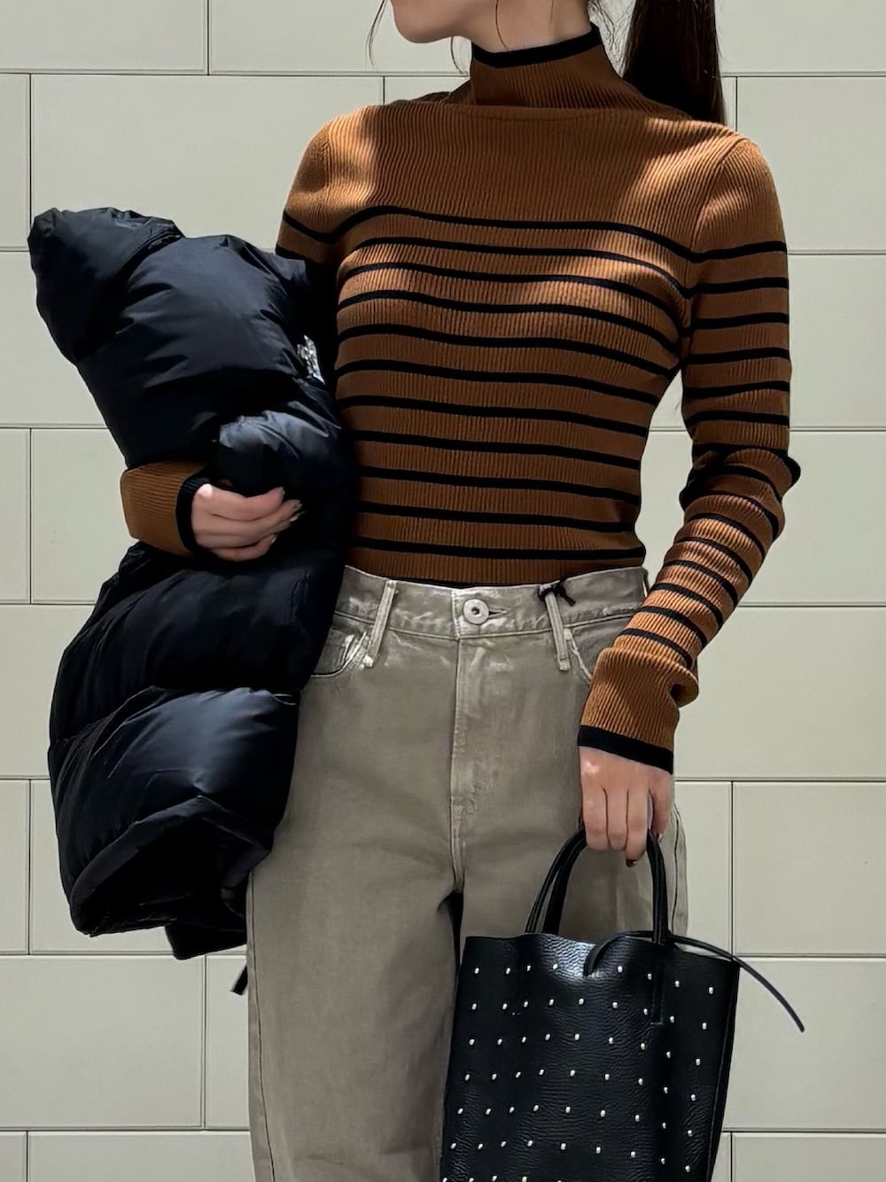 ブラウン系のニット/セーター、ブラック系のダウンジャケット/コート、ベージュ系のデニムパンツを着用したレディースの秋コーディネートの6枚目の写真