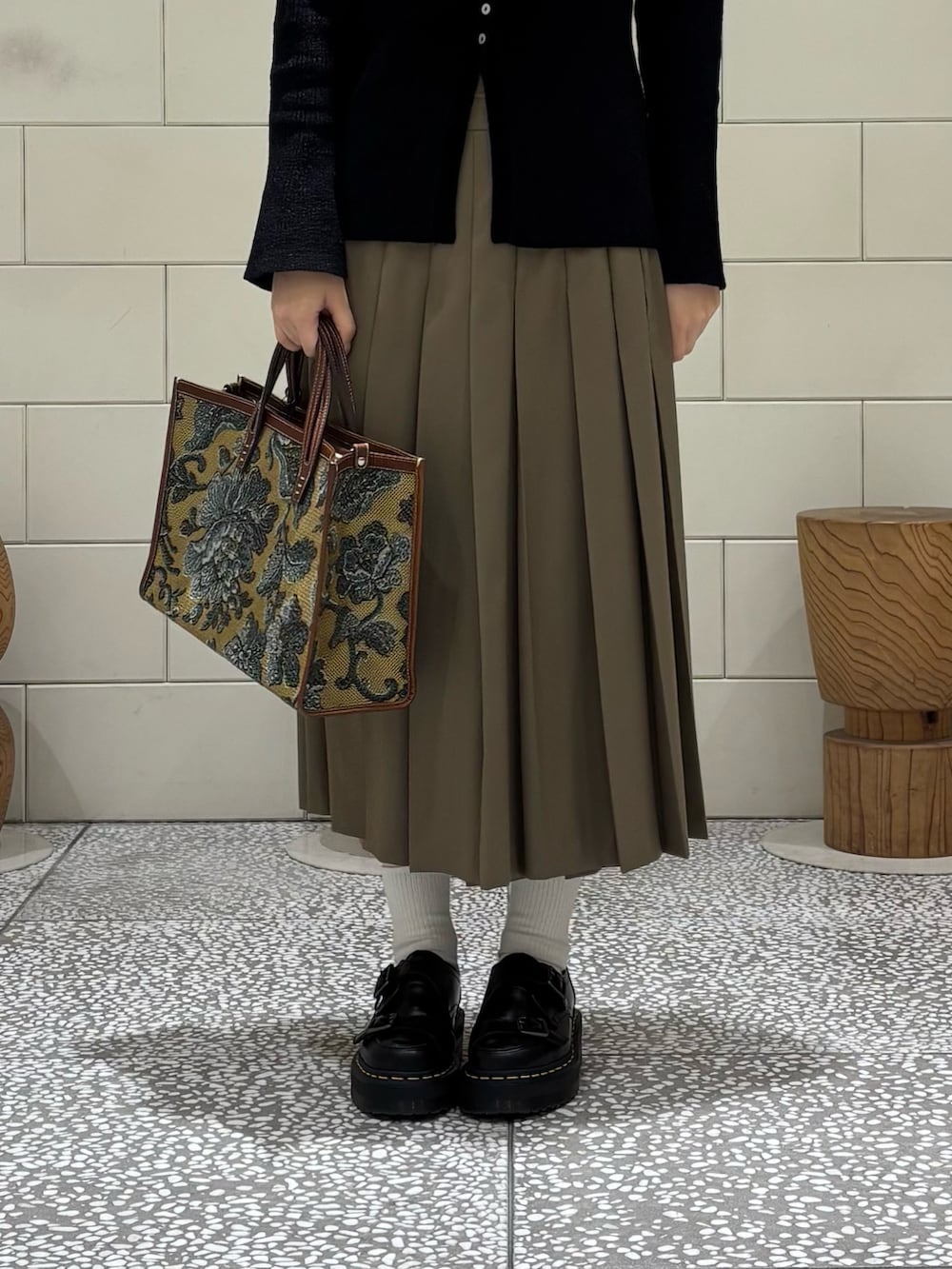 ブラック系のカーディガン/ボレロ、グリーン系のスカート、ブラウン系のハンドバッグを着用したレディースの秋コーディネートの5枚目の写真