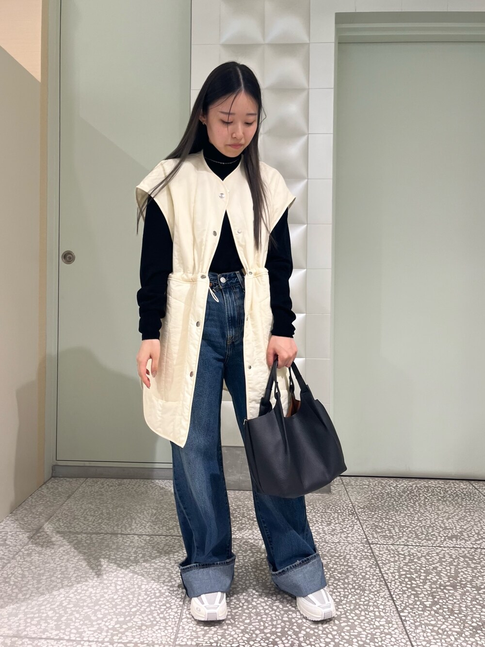 ホワイト系のダウンベスト、ブラック系のニット/セーター、ブルー系のデニムパンツを着用したレディースの秋コーディネートの2枚目の写真