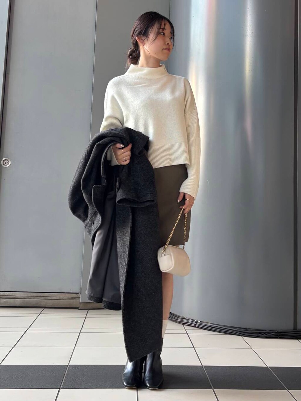 ブラック系のステンカラーコート、ホワイト系のショルダーバッグ、ブラウン系のスカートを着用したレディースの冬コーディネートの5枚目の写真