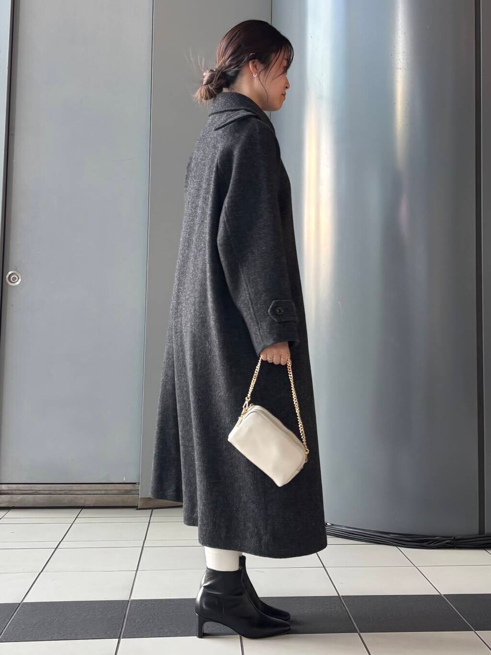 ブラック系のステンカラーコート、ホワイト系のショルダーバッグ、ブラウン系のスカートを着用したレディースの冬コーディネートの2枚目の写真