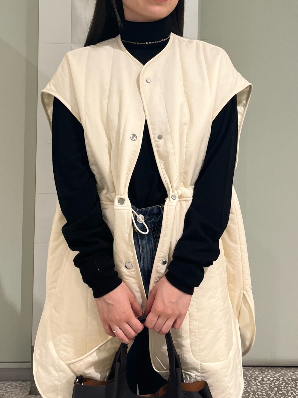 ホワイト系のダウンベスト、ブラック系のニット/セーター、ブルー系のデニムパンツを着用したレディースの秋コーディネートの5枚目の写真