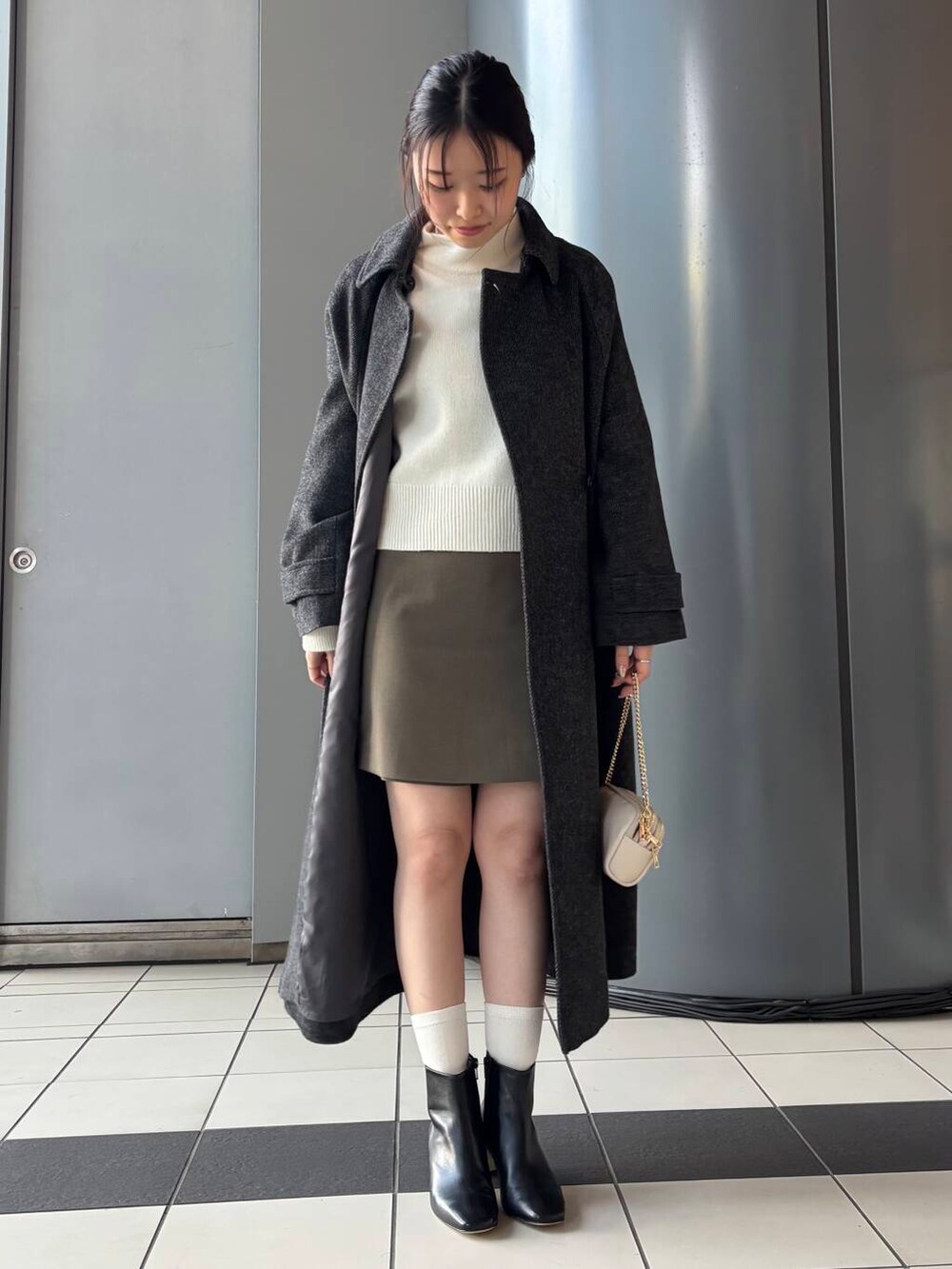 ブラック系のステンカラーコート、ホワイト系のショルダーバッグ、ブラウン系のスカートを着用したレディースの冬コーディネートの4枚目の写真
