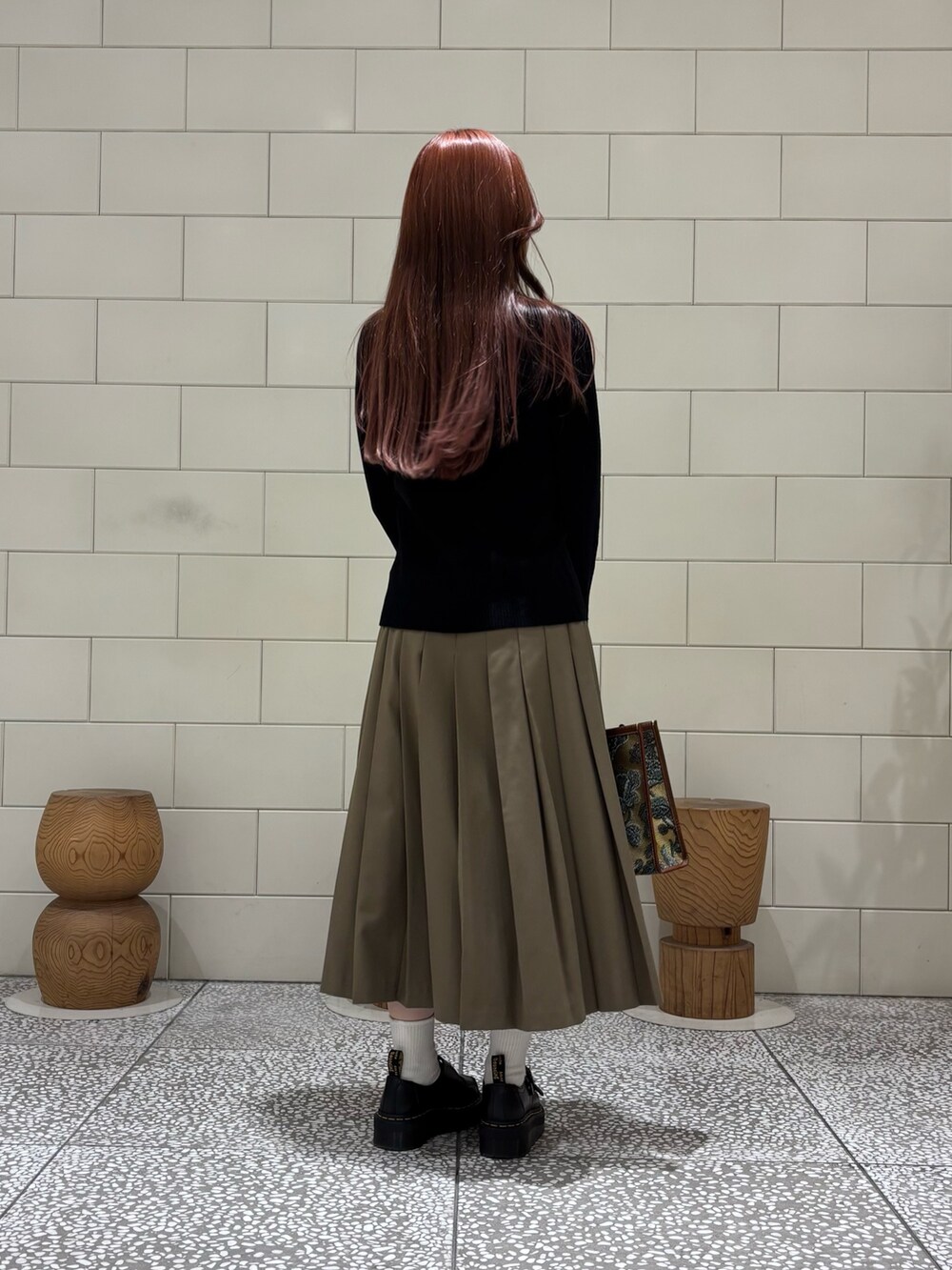 ブラック系のカーディガン/ボレロ、グリーン系のスカート、ブラウン系のハンドバッグを着用したレディースの秋コーディネートの2枚目の写真