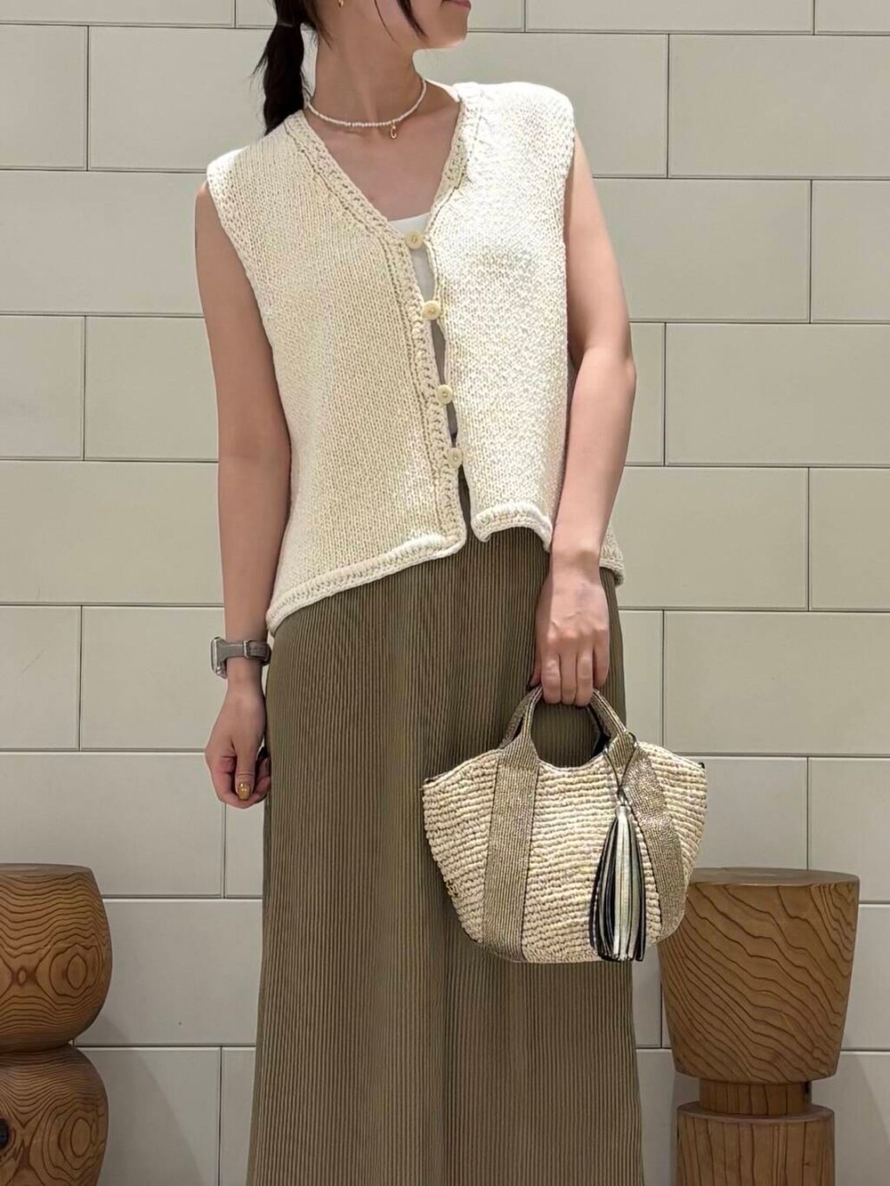 ゴールド系のかごバッグ、ホワイト系のベスト、ベージュ系のスカートを着用したレディースの夏コーディネートの4枚目の写真