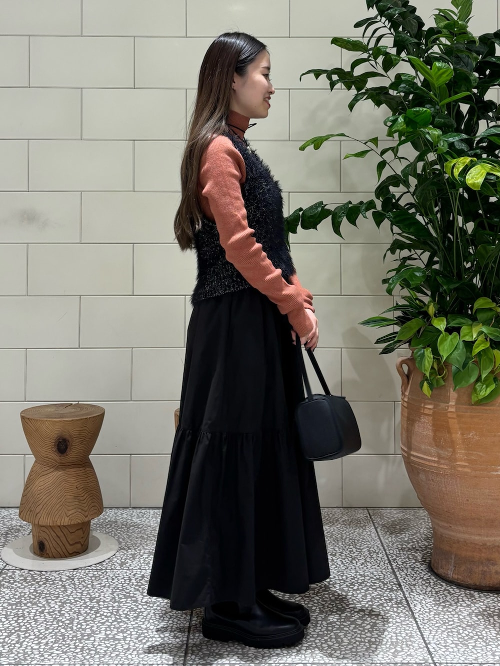 オレンジ系のニット/セーター、ブラック系のベスト、ブラック系のハンドバッグを着用したレディースの秋コーディネートの3枚目の写真