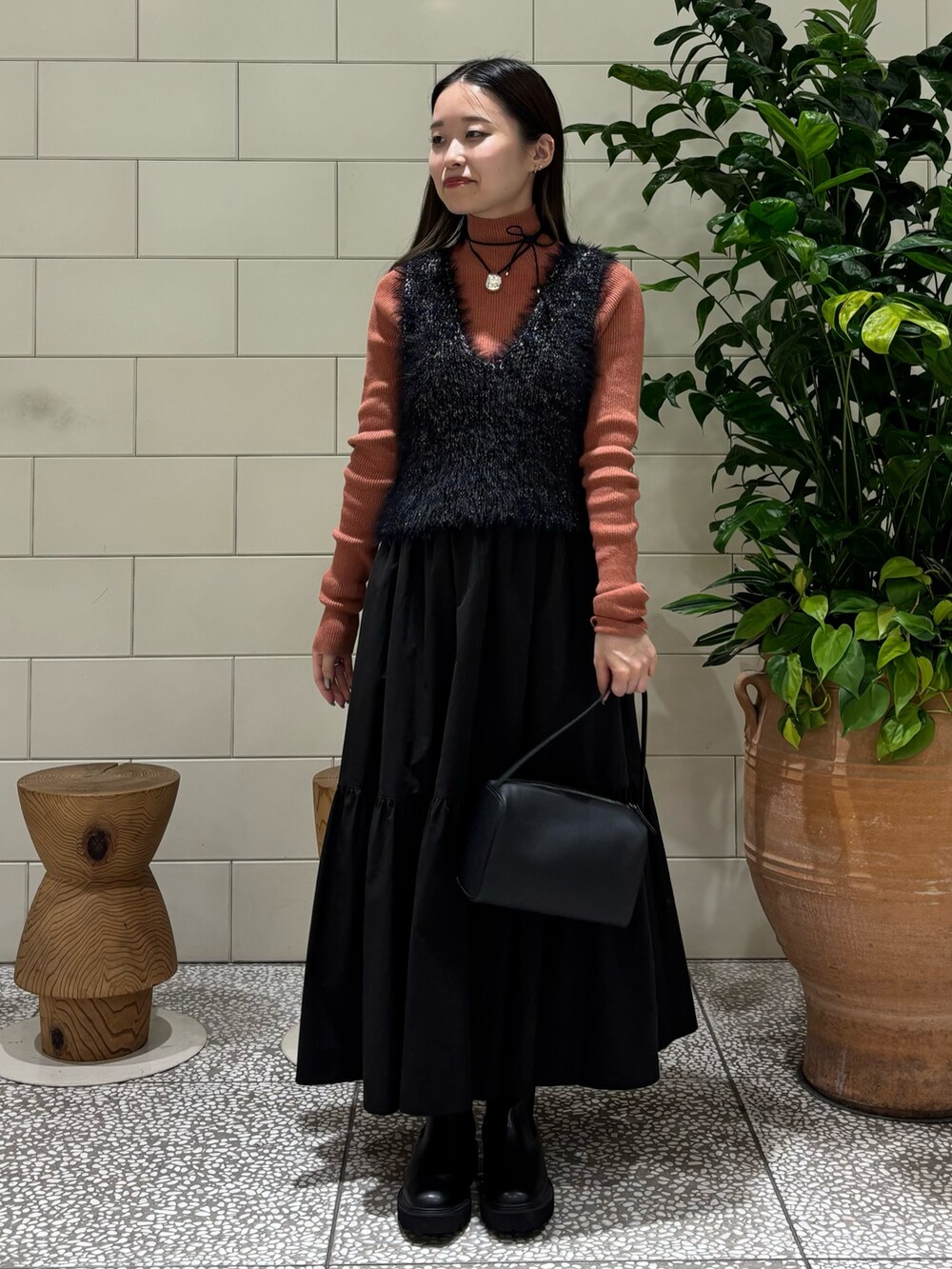オレンジ系のニット/セーター、ブラック系のベスト、ブラック系のハンドバッグを着用したレディースの秋コーディネートの2枚目の写真