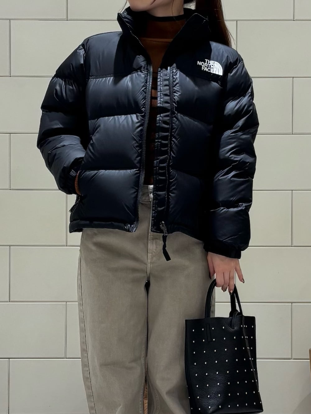 ブラウン系のニット/セーター、ブラック系のダウンジャケット/コート、ベージュ系のデニムパンツを着用したレディースの秋コーディネートの5枚目の写真