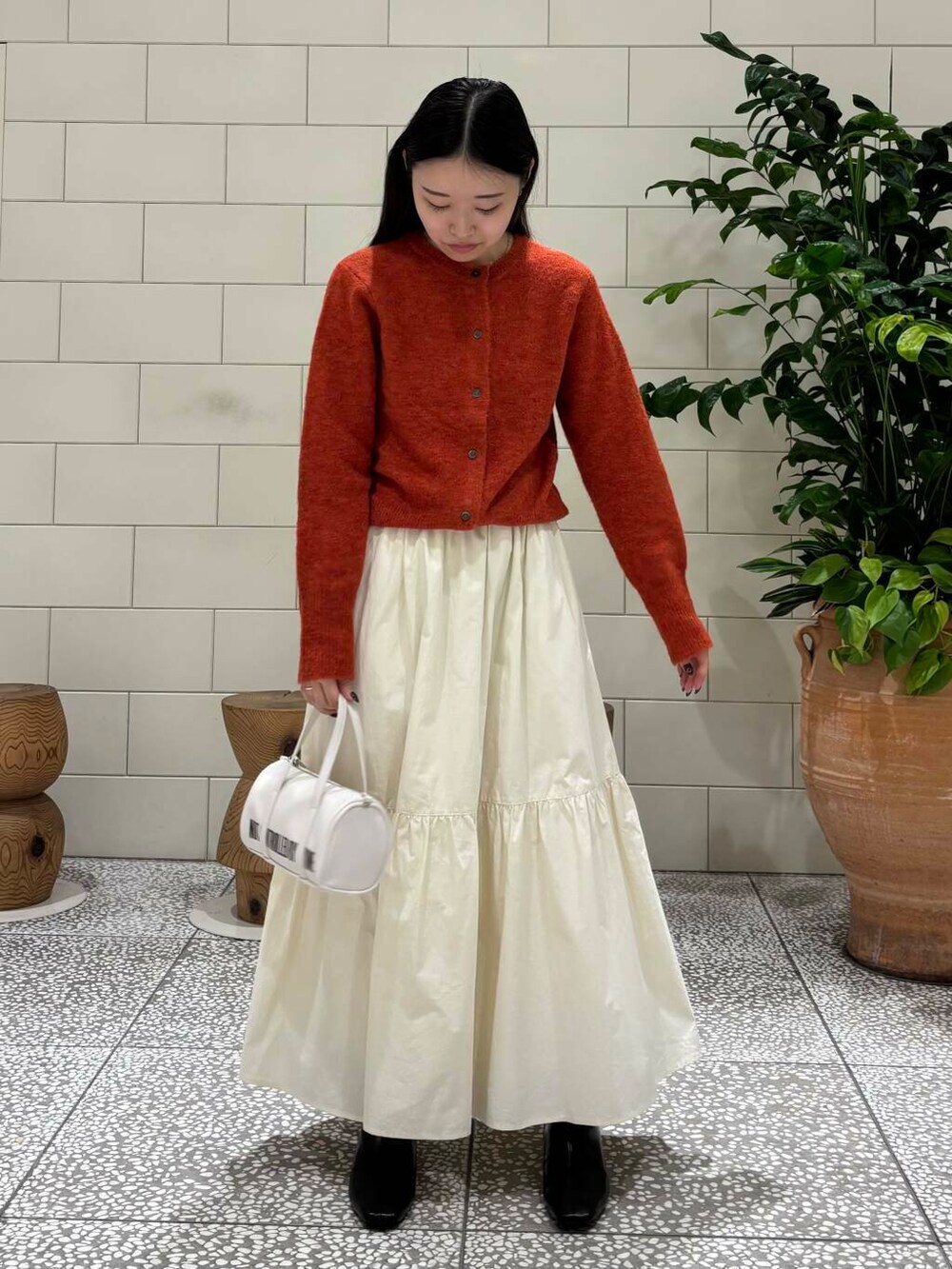 ホワイト系のスカート、ホワイト系のボストンバッグ、ブラック系のブーツを着用したレディースの秋コーディネートの2枚目の写真