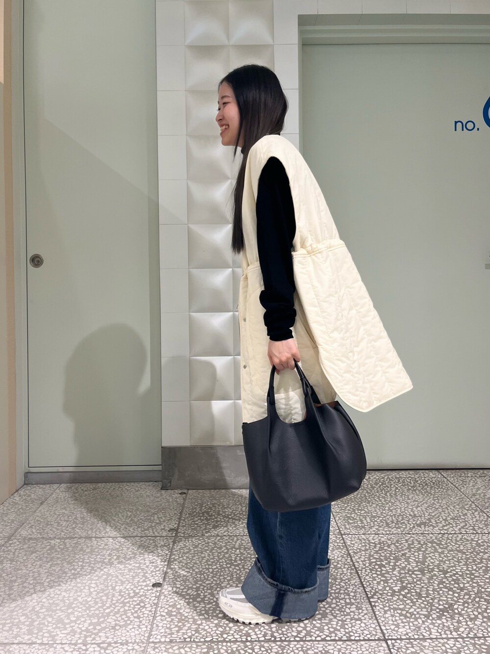 ホワイト系のダウンベスト、ブラック系のニット/セーター、ブルー系のデニムパンツを着用したレディースの秋コーディネートの3枚目の写真