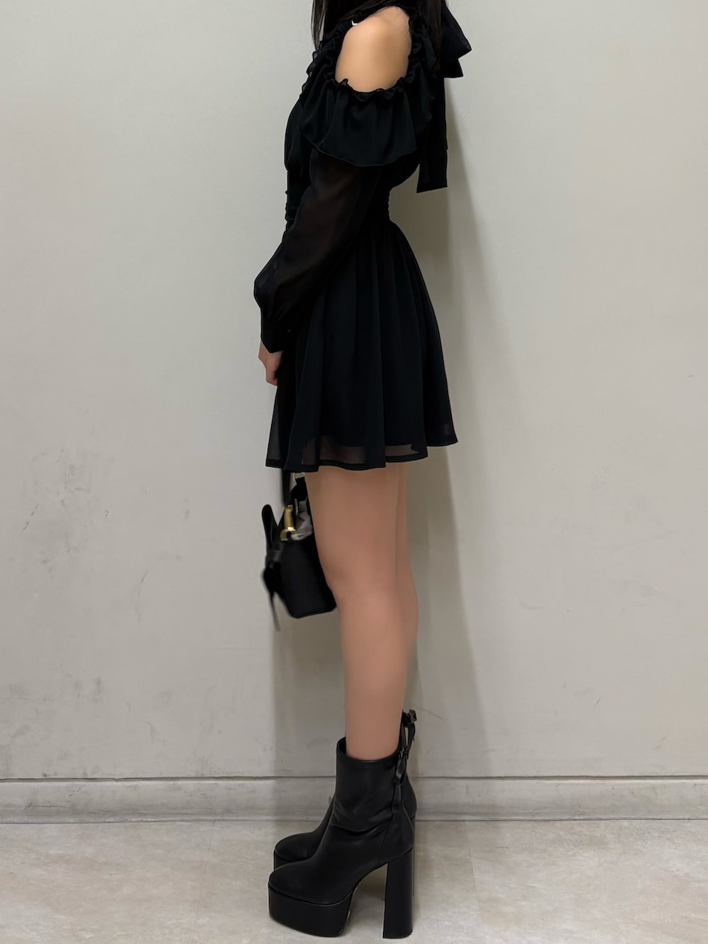 ブラック系のワンピース、ブラック系のブーツ、ブラック系のハンドバッグを着用したレディースの春コーディネートの2枚目の写真