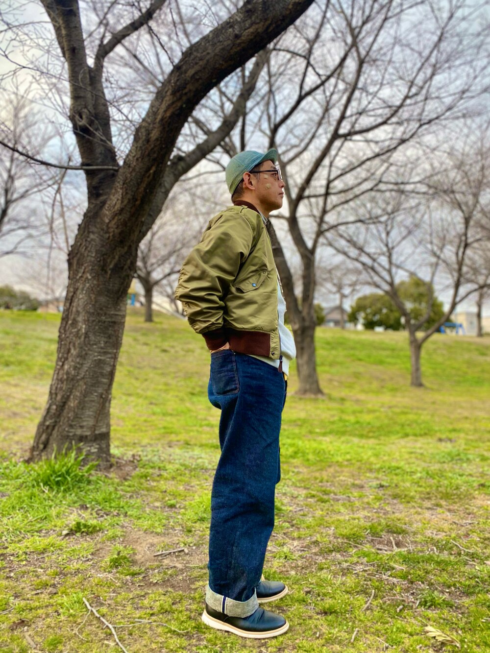 グリーン系のミリタリージャケット、グレー系のスウェット、ブルー系のデニムパンツを着用したメンズの春コーディネートの3枚目の写真