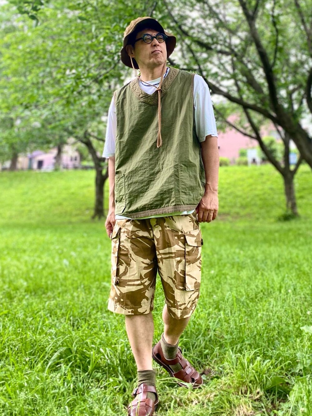 グリーン系のベスト、イエロー系のその他パンツ、ブラウン系のサンダルを着用したメンズの春コーディネートの2枚目の写真