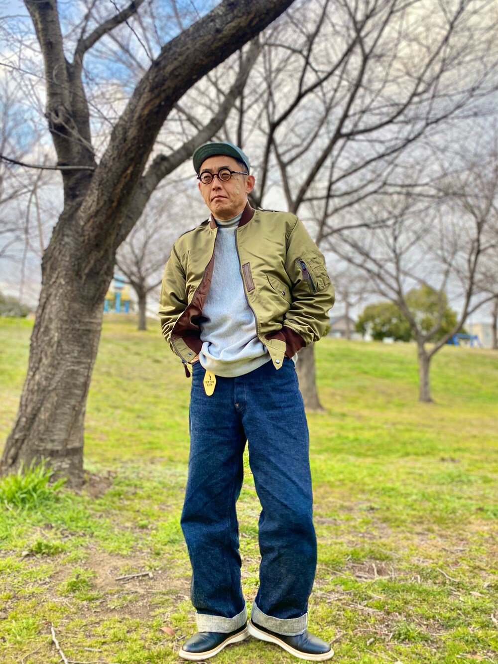 グリーン系のミリタリージャケット、グレー系のスウェット、ブルー系のデニムパンツを着用したメンズの春コーディネートの2枚目の写真