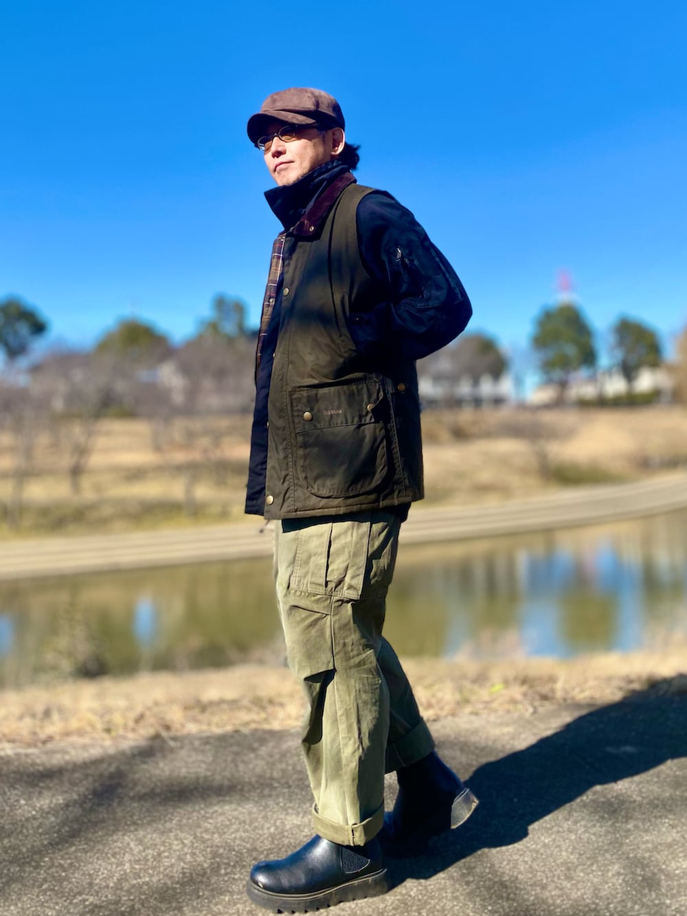 ブラウン系のベスト、ブラック系のミリタリージャケット、グリーン系のカーゴパンツを着用したメンズの冬コーディネートの2枚目の写真