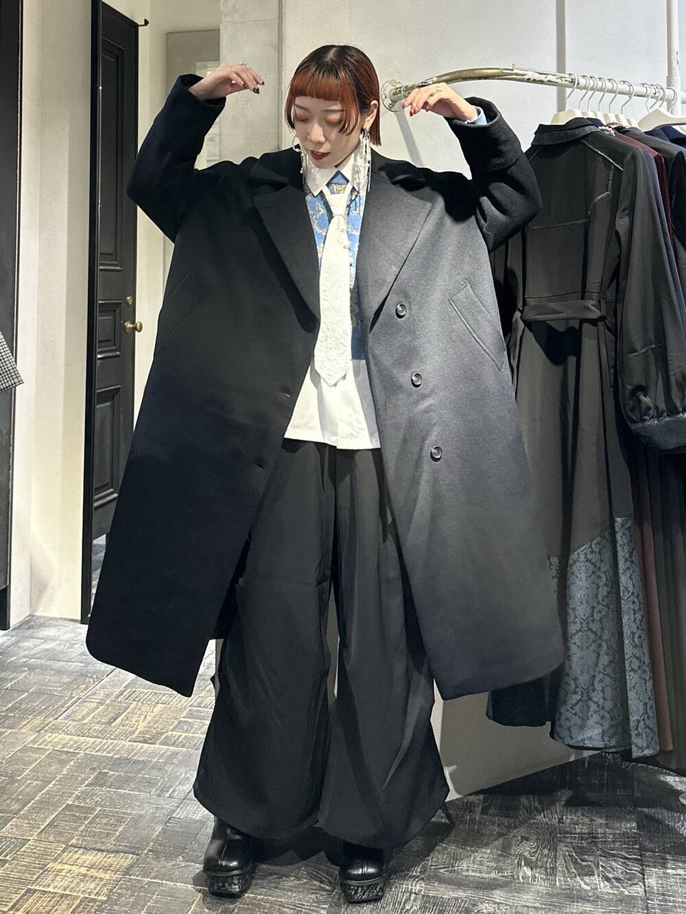 ブラック系のチェスターコート、ブルー系のニット/セーター、グレー系のブーツを着用したレディースの秋コーディネートの5枚目の写真