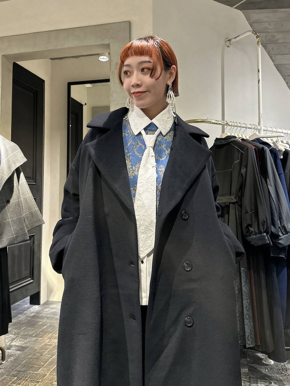 ブラック系のチェスターコート、ブルー系のニット/セーター、グレー系のブーツを着用したレディースの秋コーディネートの2枚目の写真