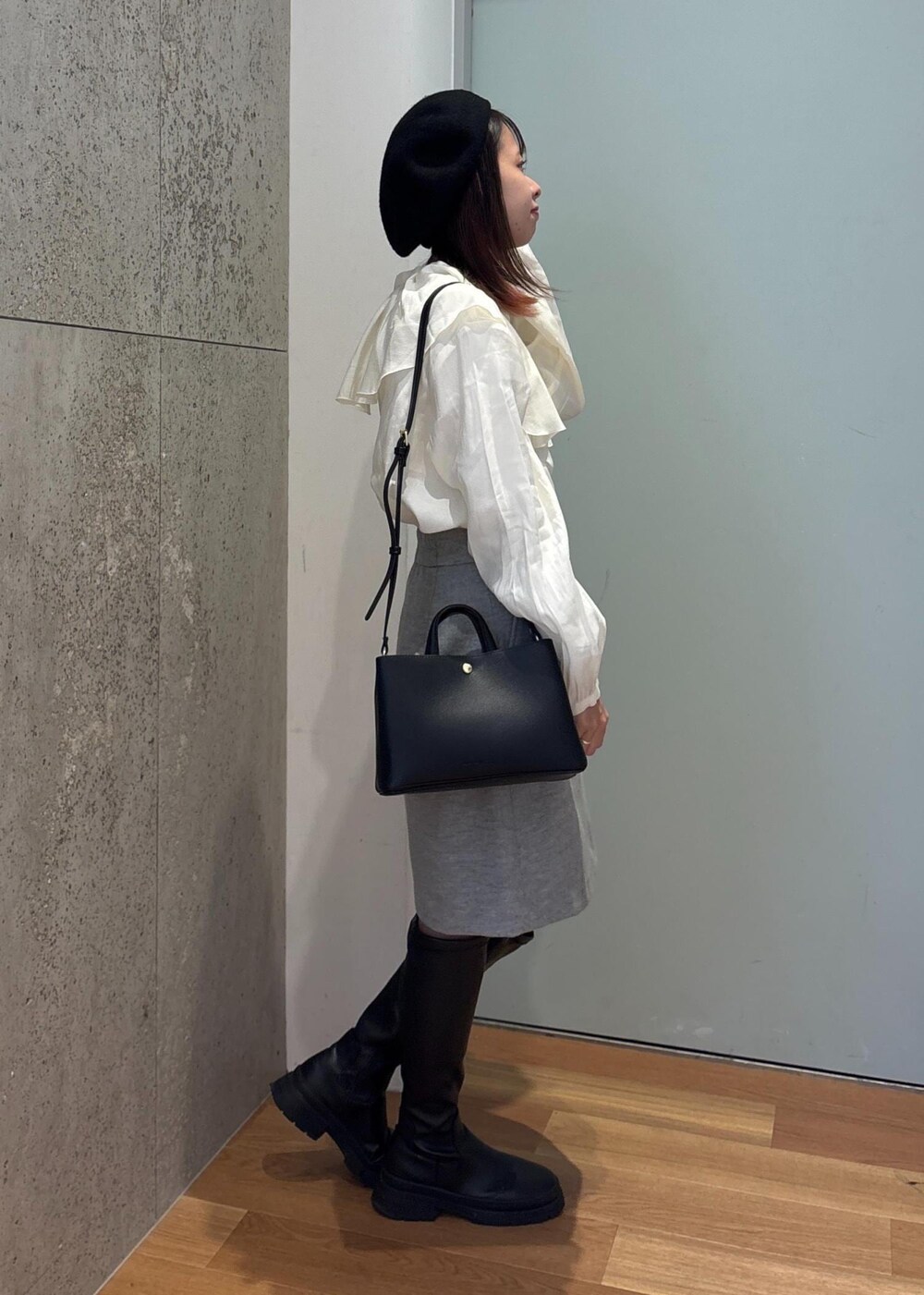 グレー系のスカート、ホワイト系のシャツ/ブラウス、ブラック系のブーツを着用したレディースの冬コーディネートの2枚目の写真