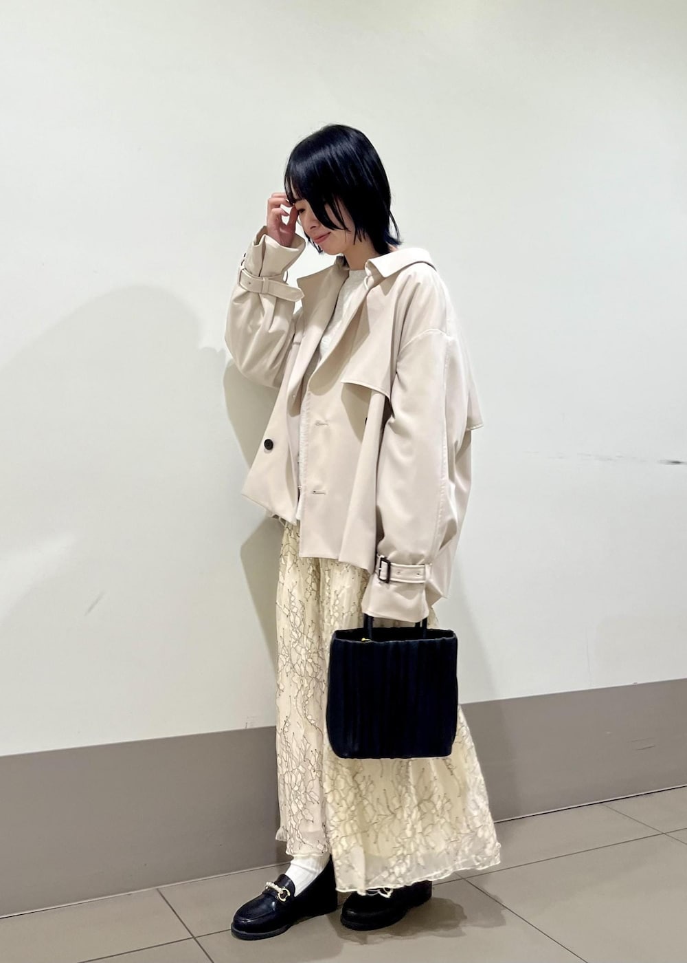 ブラック系のローファー、ホワイト系のスカート、ベージュ系のトレンチコートを着用したレディースの春コーディネートの3枚目の写真