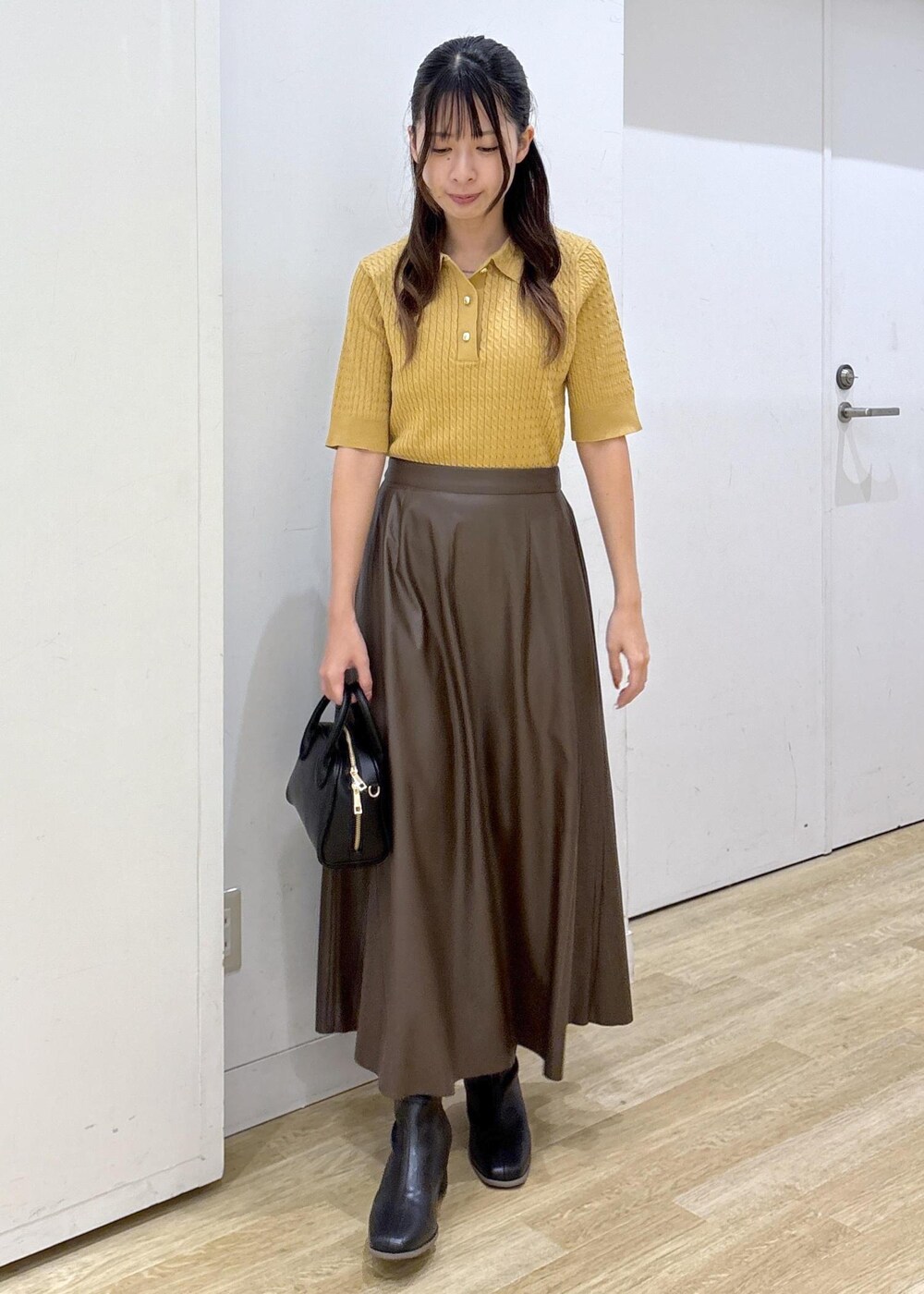 ブラウン系のスカート、イエロー系のポロシャツ、ブラック系のショルダーバッグを着用したレディースの秋コーディネートの2枚目の写真