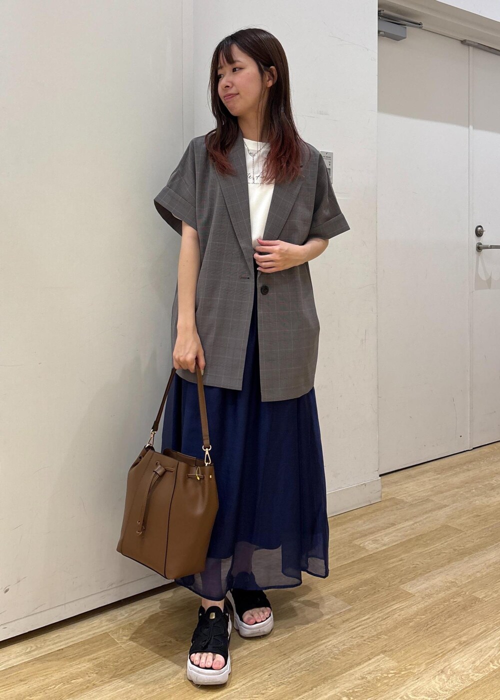 グレー系のテーラードジャケット、ブラウン系のショルダーバッグ、ブルー系のスカートを着用したレディースの夏コーディネートの2枚目の写真