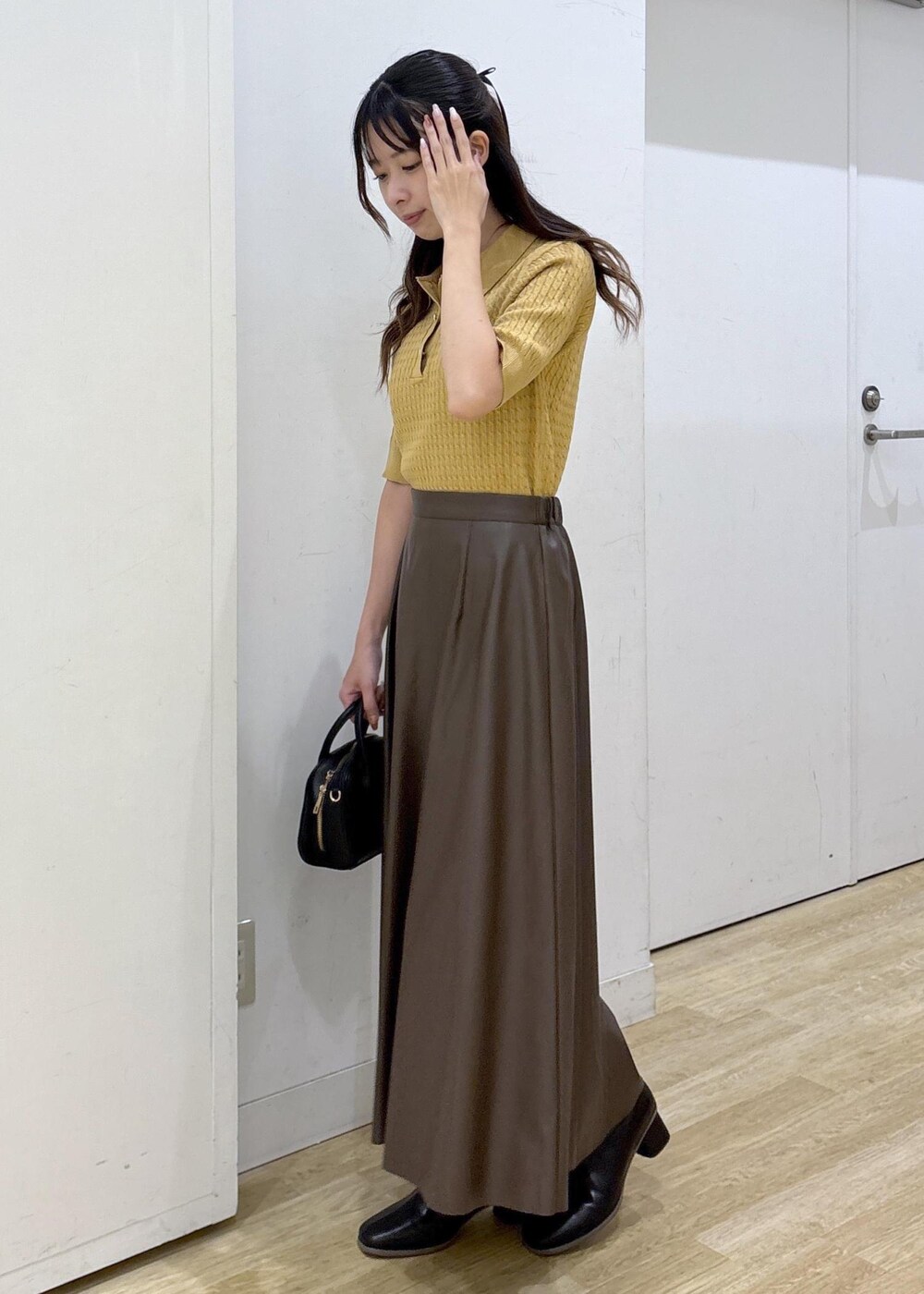 ブラウン系のスカート、イエロー系のポロシャツ、ブラック系のショルダーバッグを着用したレディースの秋コーディネートの5枚目の写真