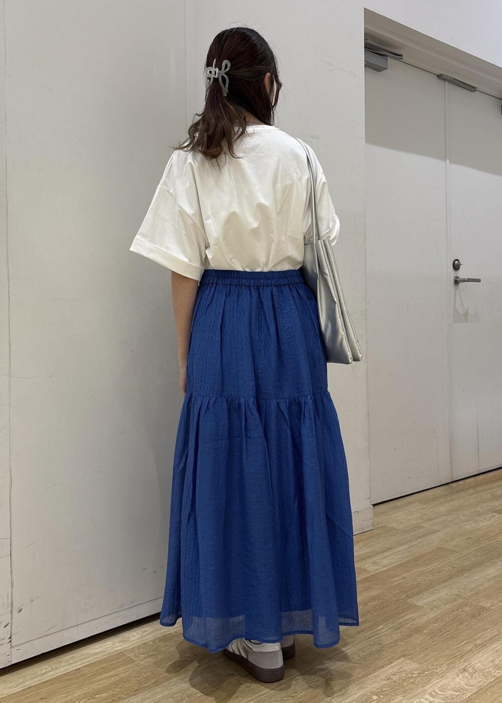 シルバー系のトートバッグ、ブルー系のスカート、ホワイト系のTシャツ/カットソーを着用したレディースの夏コーディネートの5枚目の写真