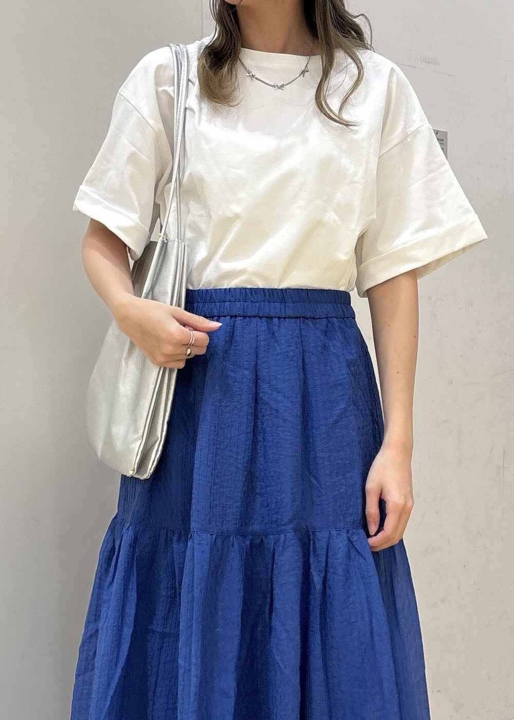 シルバー系のトートバッグ、ブルー系のスカート、ホワイト系のTシャツ/カットソーを着用したレディースの夏コーディネートの6枚目の写真