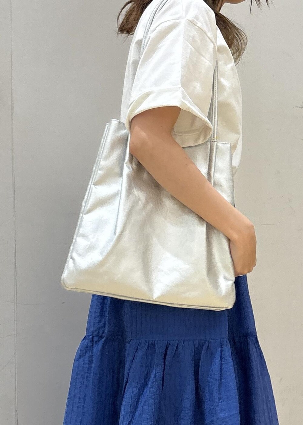 シルバー系のトートバッグ、ブルー系のスカート、ホワイト系のTシャツ/カットソーを着用したレディースの夏コーディネートの7枚目の写真