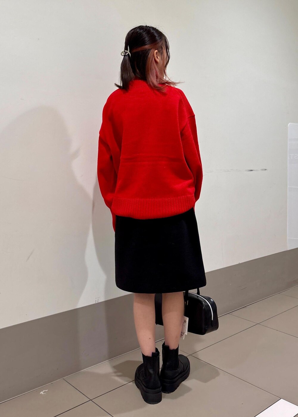 レッド系のニット/セーター、ブラック系のボストンバッグ、ブラック系のスカートを着用したレディースの冬コーディネートの3枚目の写真