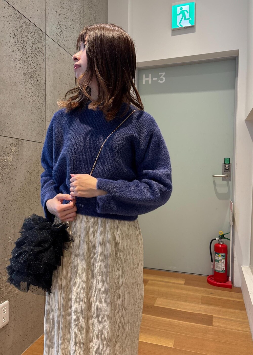 ブルー系のニット/セーター、ブラック系のショルダーバッグ、ホワイト系のスカートを着用したレディースの春コーディネートの6枚目の写真