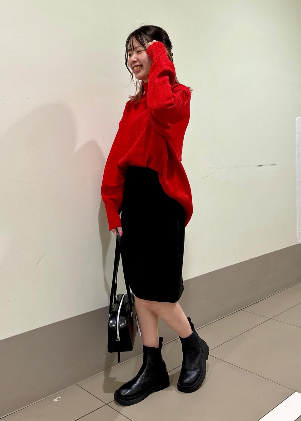 レッド系のニット/セーター、ブラック系のボストンバッグ、ブラック系のスカートを着用したレディースの冬コーディネートの2枚目の写真