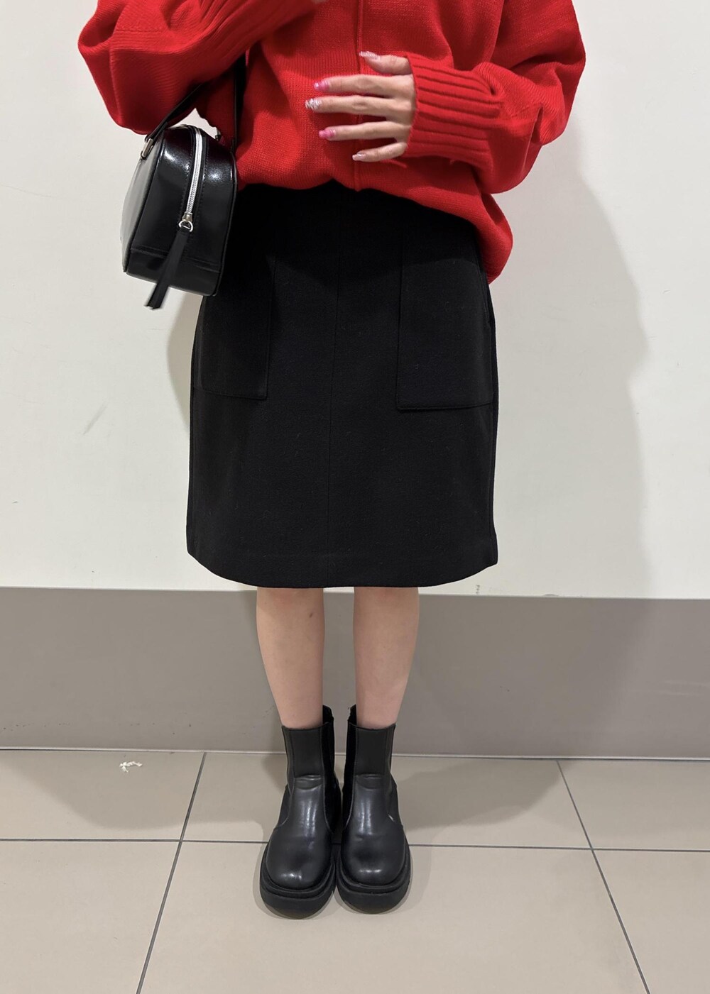 レッド系のニット/セーター、ブラック系のボストンバッグ、ブラック系のスカートを着用したレディースの冬コーディネートの7枚目の写真