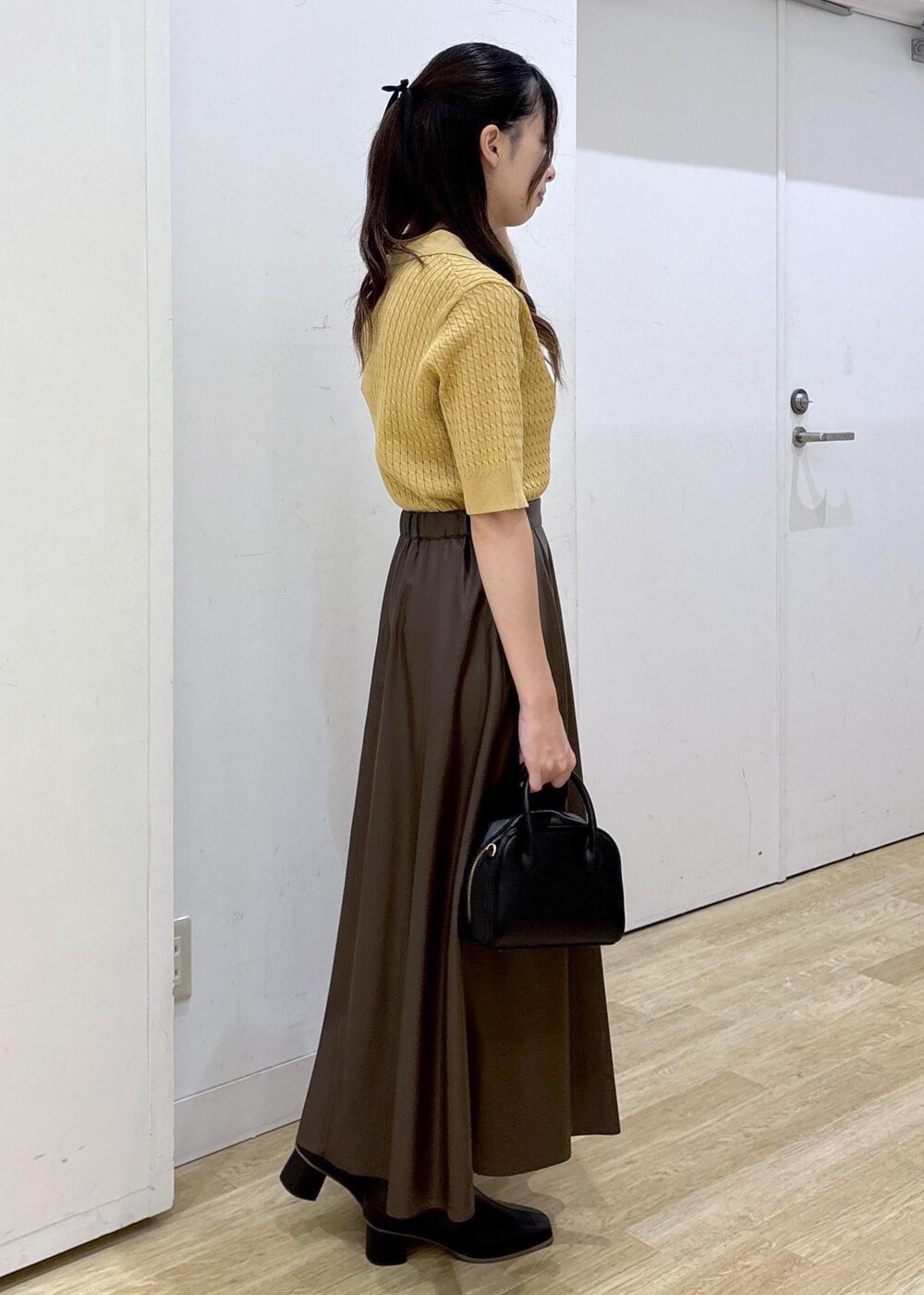 ブラウン系のスカート、イエロー系のポロシャツ、ブラック系のショルダーバッグを着用したレディースの秋コーディネートの3枚目の写真