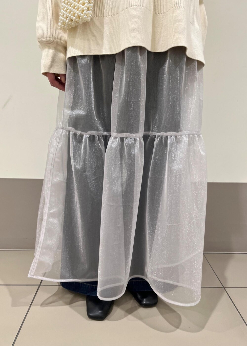 ホワイト系のショルダーバッグ、ブルー系のデニムパンツ、グレー系のスカートを着用したレディースの春コーディネートの5枚目の写真