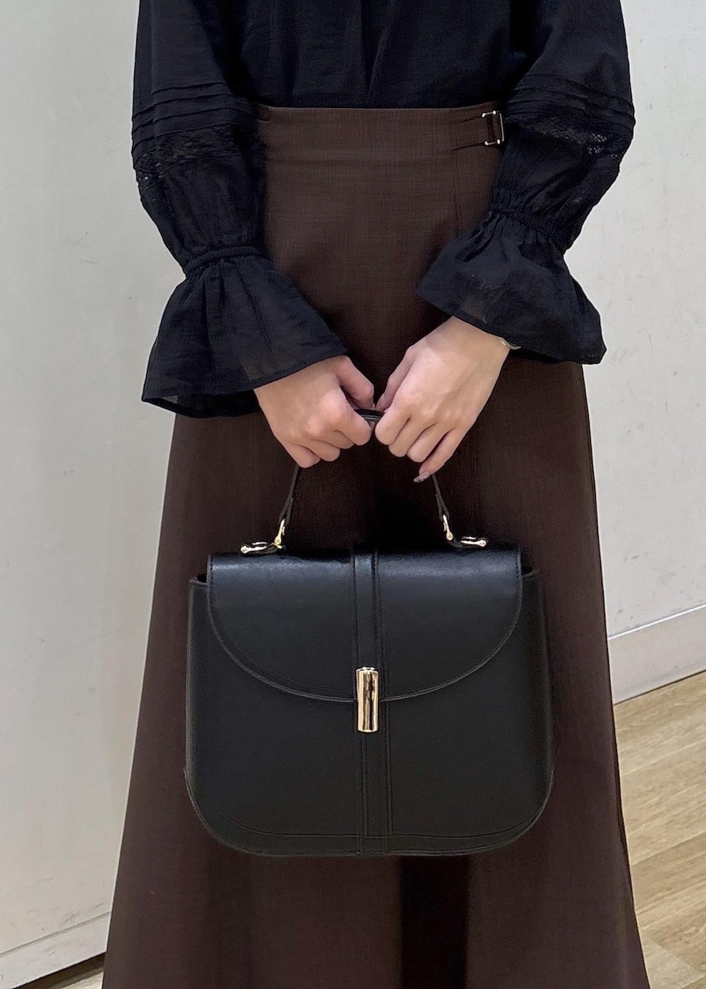 ブラック系のショルダーバッグ、ブラウン系のスカート、ブラック系のシャツ/ブラウスを着用したレディースの春コーディネートの7枚目の写真