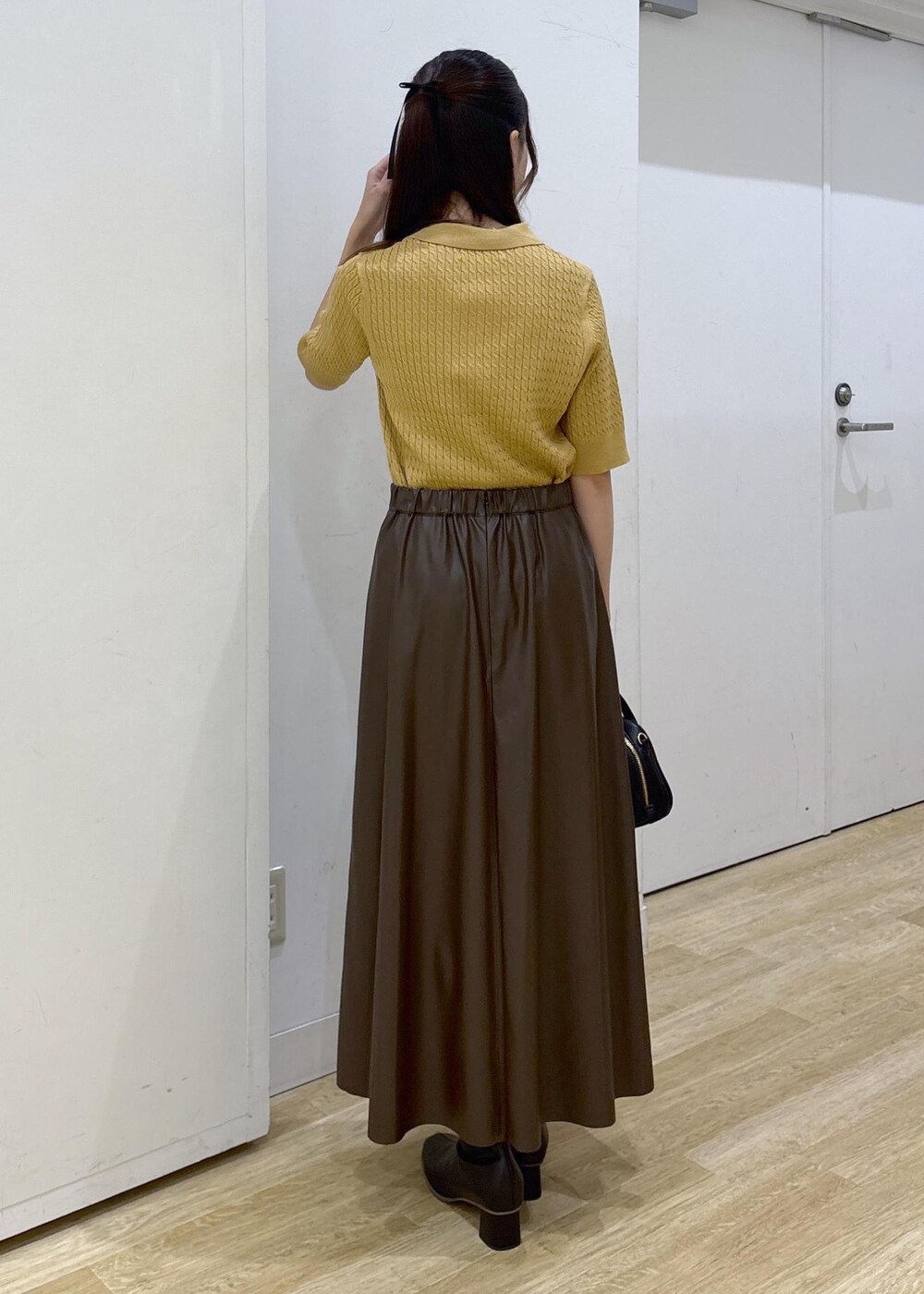 ブラウン系のスカート、イエロー系のポロシャツ、ブラック系のショルダーバッグを着用したレディースの秋コーディネートの4枚目の写真